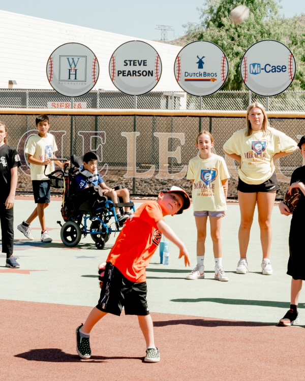Two young kids practicing baseball on the field, with one of them using a walker while others are on the field in a playful stance. Featured in Scottsdale Lifestyle Magazine.